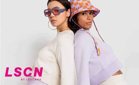 LSCN by Lascana – Zwei Frauen in lässigen Outfits, eine mit hellen Pullover, die andere mit lila Oberteil und kariertem Hut.