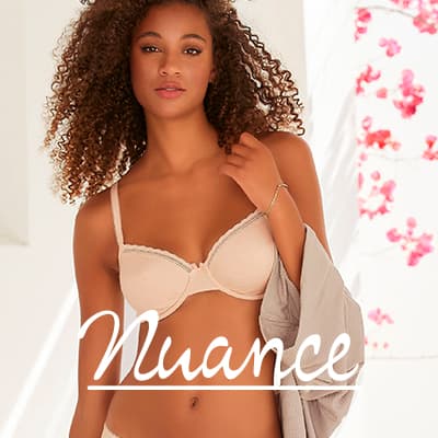 Nuance – Frau in hellen Dessous steht im Licht, hält ein offenes Hemd und blickt ruhig in die Kamera