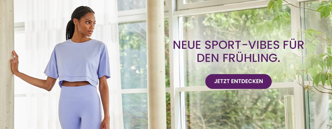 Neue Sport-Vibes für den Frühling – Frau in lila Sportoutfit steht im hellen Raum vor großen Fenstern mit Pflanzen