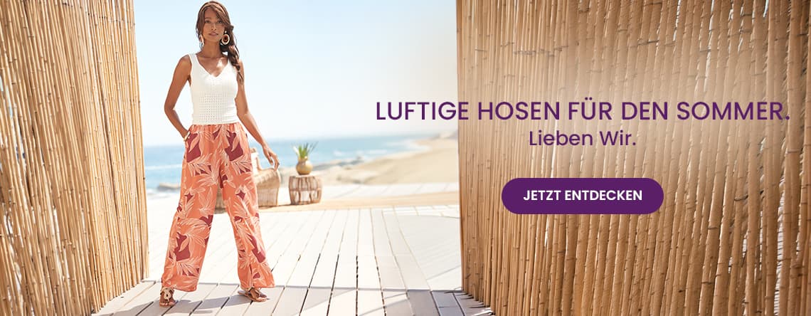 Luftige Hosen für den Sommer – Frau in weiter gemusterter Hose steht barfuß auf Holzsteg mit Blick auf Strand und Meer