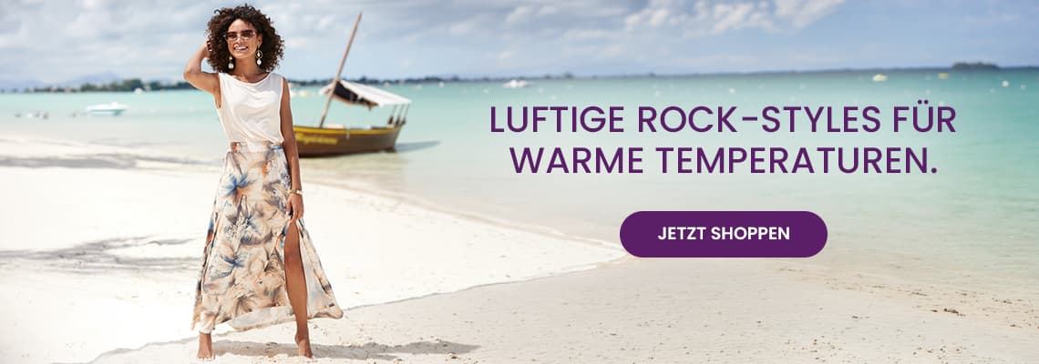 Luftige Rock-Styles für warme Temperaturen – Frau im gemusterten Maxirock steht am Strand vor ruhigem Meer
